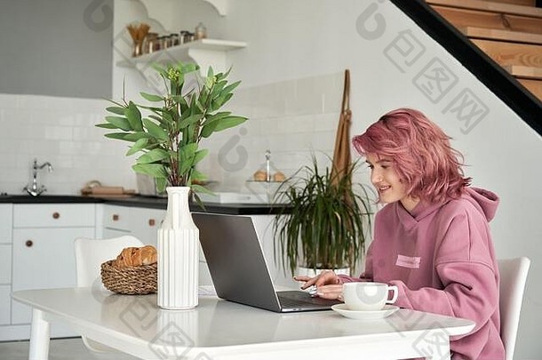 快乐青少年女孩粉红色的头发移动PC坐厨房表格早餐