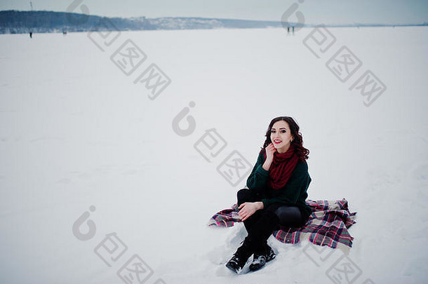 浅黑肤色的女人女孩绿色毛衣红色的围巾坐着格子户外冻湖晚上冬天一天