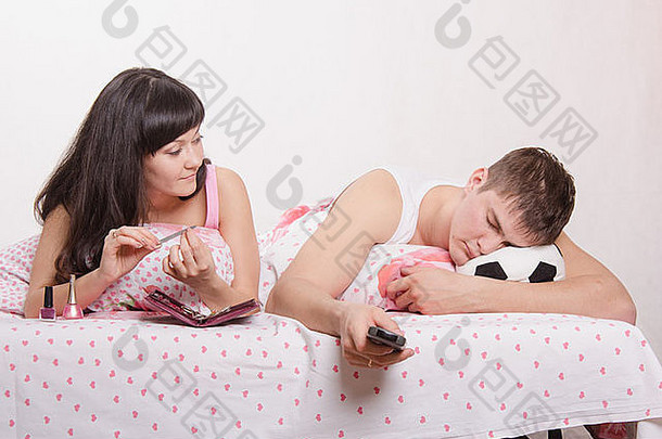 年轻的女孩的家伙床上美丽的女孩修指甲男人。看足球