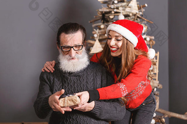 有吸引力的长头发的女儿红色的毛衣穿圣诞老人他微笑圣诞节礼物有胡子的高级爸爸穿眼镜灰色的毛衣惊讶快乐一年圣诞节假期记忆礼物购物折扣商店雪少女圣诞老人老人化妆发型狂欢节