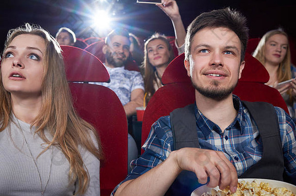 前面视图夫妇吃爆米花屏幕电影剧院红色的椅子金发女郎女孩灰色的英俊的男人。浪漫的日期享受有趣的电影