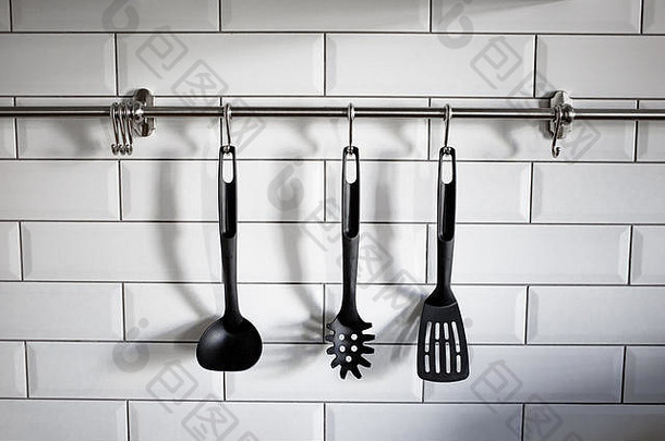 黑色的塑料厨房用具挂白色石头墙照片炊具厨房餐具挂白色砖背景
