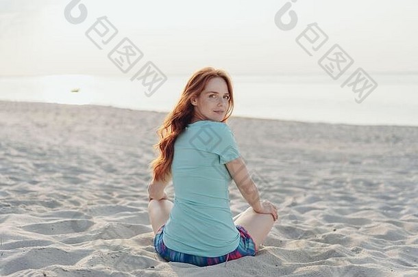 年轻的女人坐着海滩回来肩膀引人发笑的表达式相机