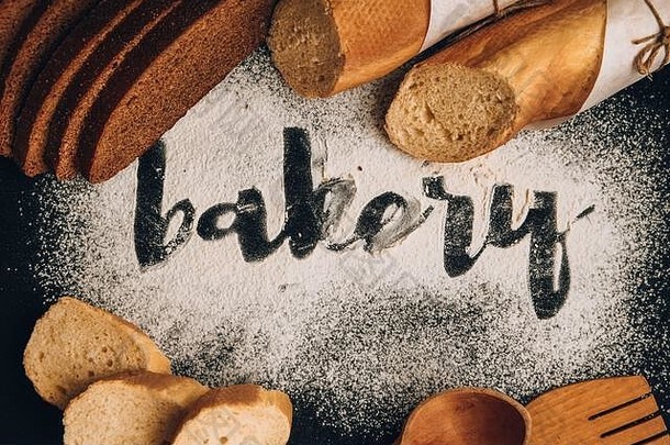 登记面包店白色小麦面粉分散切片法国魔杖黑麦面包木勺子黑暗背景