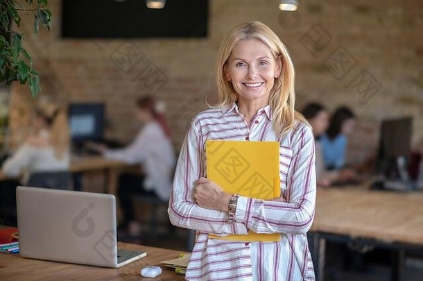 金发女郎女人站办公室持有黄色的文件夹