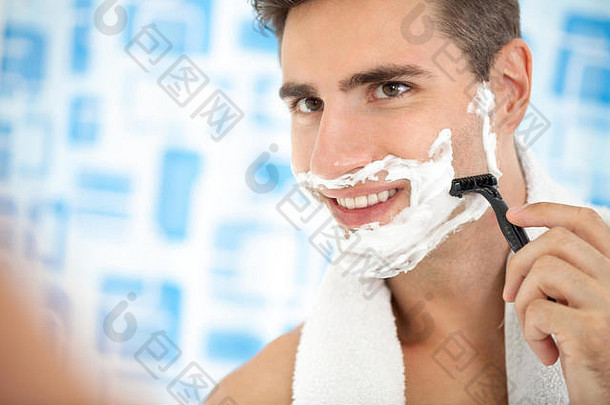 年轻的男人。剃须胡子剃须刀反映了浴室的镜子