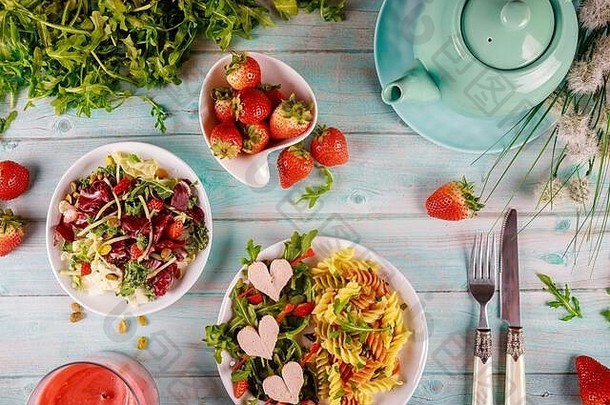 节日情人节一天晚餐色彩斑斓的面条意大利面芝麻菜沙拉草莓白色木背景