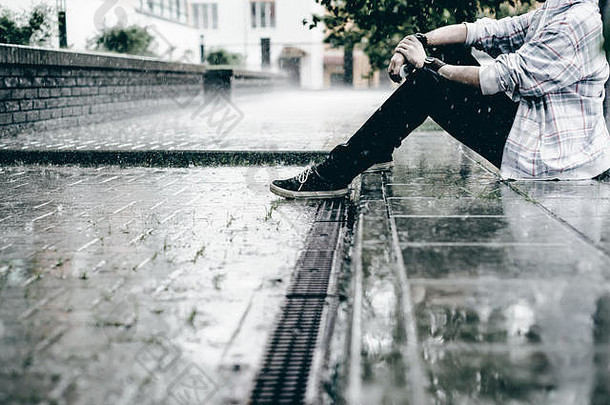 年轻的男人。胡子光网纹夹克罩帽太阳镜走自由城市坐在地面雨