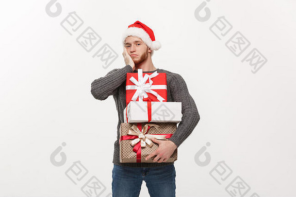 圣诞节概念年轻的英俊的男人。胡子持有重礼物疲惫面部表达式白色背景