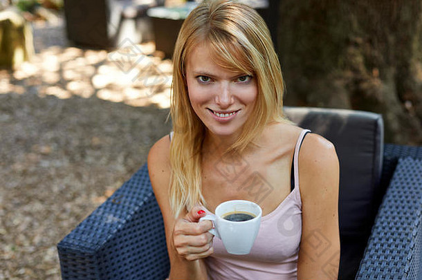美丽的年轻的女夏天衣服坐着花园扶手椅杯热咖啡相机微笑模糊背景