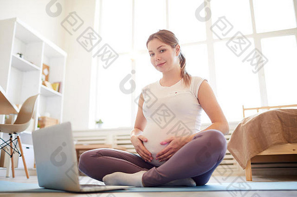 怀孕了女人坐着瑜伽席