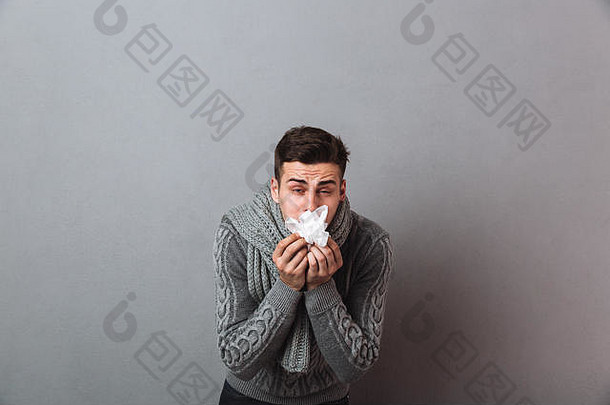 照片年轻的不高兴疾病男人。穿温暖的围巾站孤立的灰色墙持有餐巾相机
