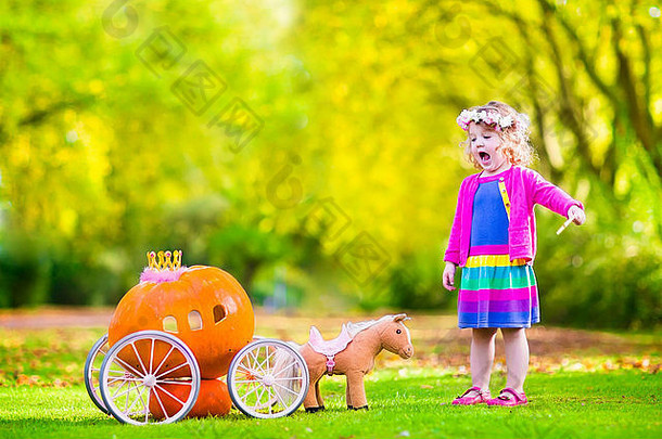 可爱的卷曲的女孩玩灰姑娘仙女演讲持有魔法魔杖南瓜马车有趣的秋天公园