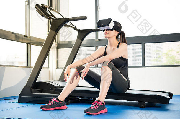 美亚洲女人休息跑步机虚拟现实耳机眼镜设备在室内健身房背景