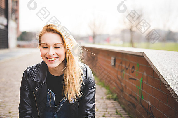 肖像年轻的美丽的金发女郎直头发女人城市相机笑穿黑色的皮革夹克日落背光无忧无虑青年概念