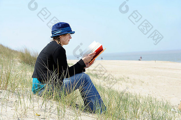 美丽的年轻的女人书坐着沙丘海滩
