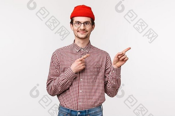 半身照肖像满意快乐微笑年轻的赶时髦的人的家伙红色的无檐小便帽眼镜指出手指前广告很高兴表达式