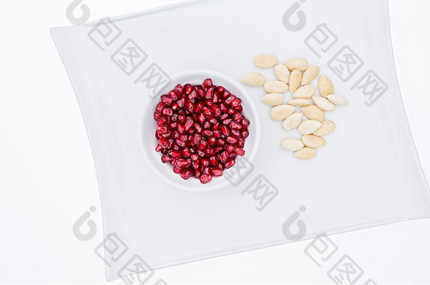 碗新鲜的成熟的红色的石榴种子去皮变白杏仁服务白色板健康的有营养的