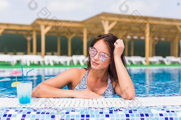 十美丽的女人比基尼桑拉斯坐着游泳池鸡尾酒时尚肖像优雅的女人比基尼太阳镜