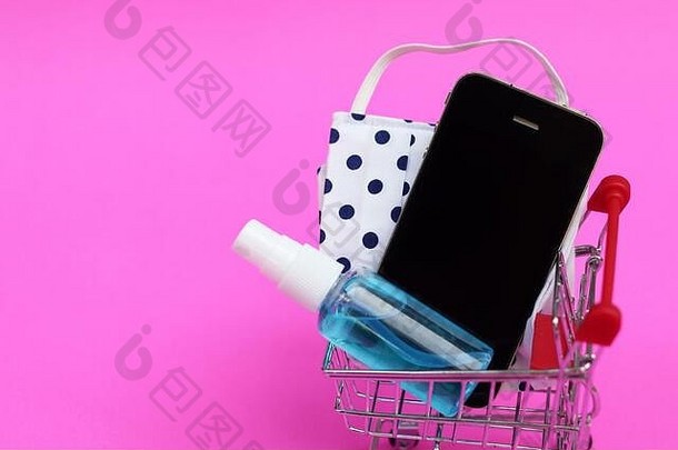 购物车脸面具手洗手液喷雾聪明的电话粉红色的背景概念正常的购物在线科维德流感大流行