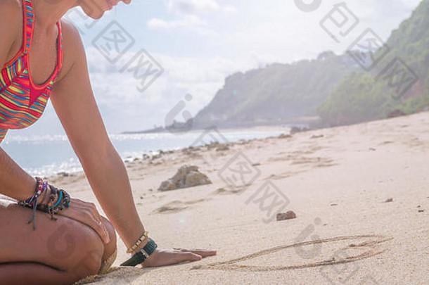 年轻的女人画心形状沙子海滩巴厘岛