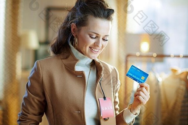 快乐年轻的女人白色毛衣裙子米色外套红色的出售价格标签持有蓝色的信贷卡现代时尚展厅