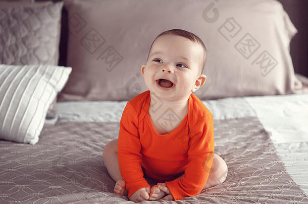 肖像可爱的可爱的高加索人微笑笑婴儿男孩女孩黑色的棕色（的）眼睛橙色红色的装衬衫坐着床上lookingaway