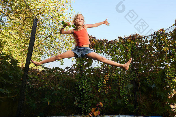 孩子可爱的金发碧眼的女孩玩跳蹦床绿色植物背景