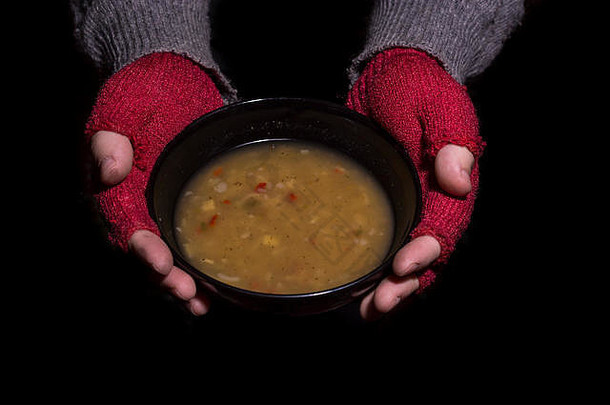 贫困概念男人。红色的手套持有碗汤孤立的黑色的背景