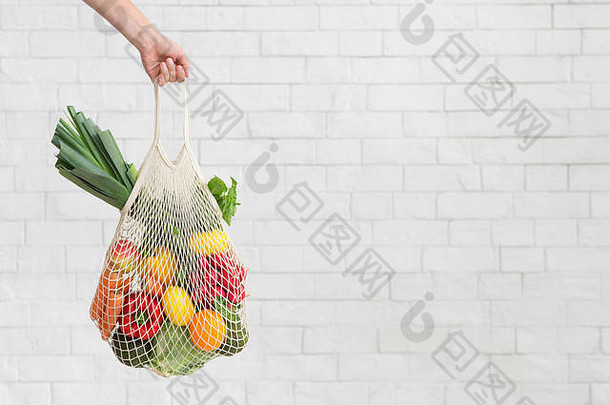 女人持有新鲜的蔬菜白色砖墙生态购物袋