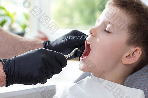 拔牛奶牙男孩坐着牙科椅子牙医黑色的橡胶<strong>手套</strong>持有一边根杆