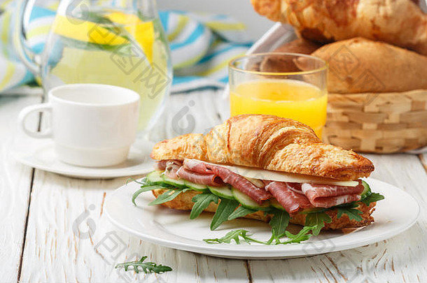 新鲜的sandwich-croissant他芝麻菜黄瓜奶酪白色板柠檬水橙色汁咖啡杯表格早餐塞莱克