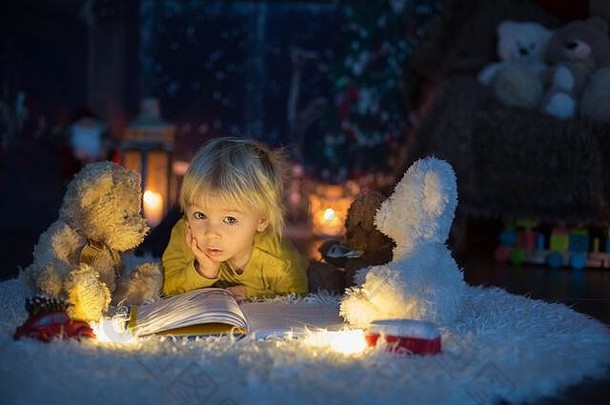 甜蜜的蹒跚学步的男孩阅读书首页晚上圣诞节晚上