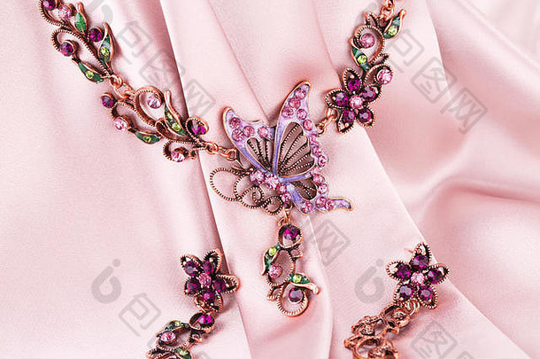 时尚的项链耳环粉红色的织物背景