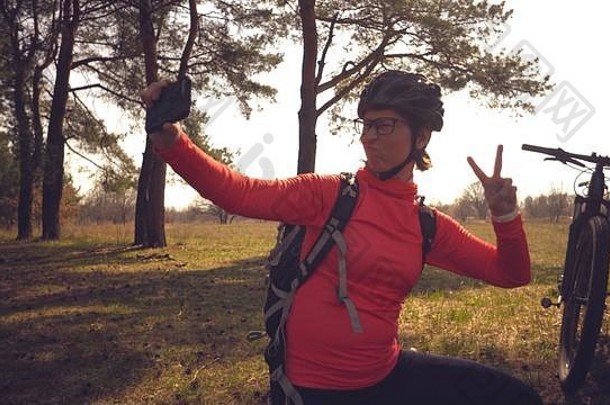 年轻的高加索人女人运动员旅游骑<strong>自行车</strong>的人手聪明的电话照片自拍坐着树松柏科的森林城市