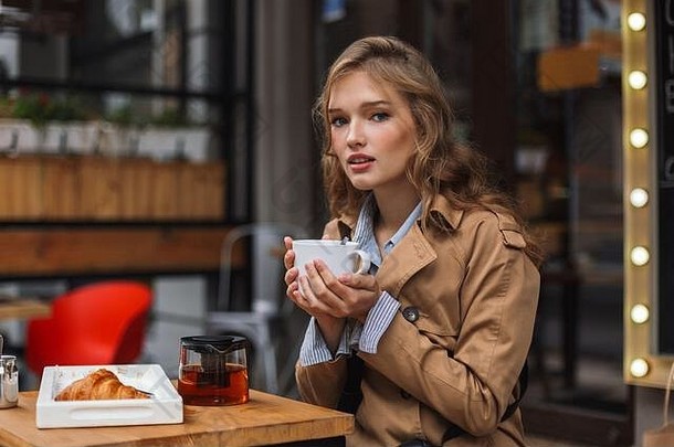 年轻的有吸引力的女人沟外套如痴如梦相机持有茶壶白色杯户外舒适的咖啡馆阳台
