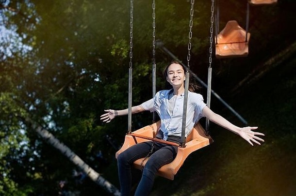 快乐孩子十几岁的女孩骑链旋转木马摇摆不定的娱乐公园