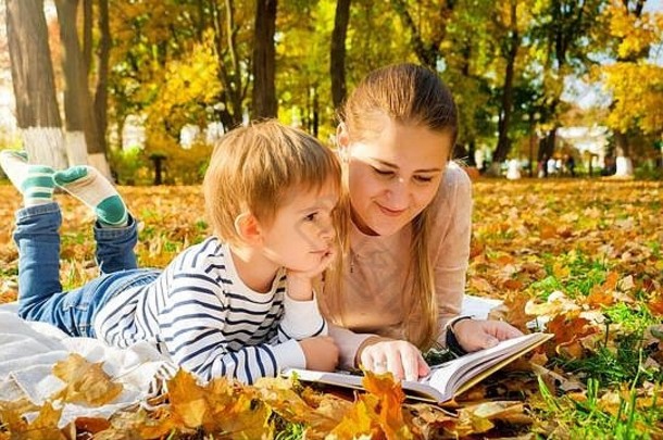 肖像男孩说谎妈妈。秋天公园阅读书