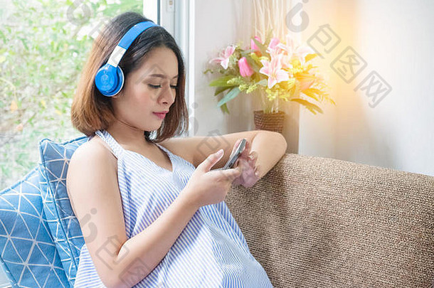 怀孕了女人移动聪明的电话坐着床上放松怀孕技术