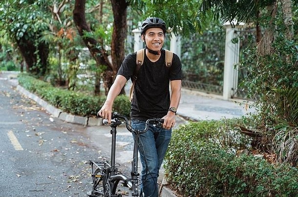 微笑亚洲年轻的男人。走折叠自行车街