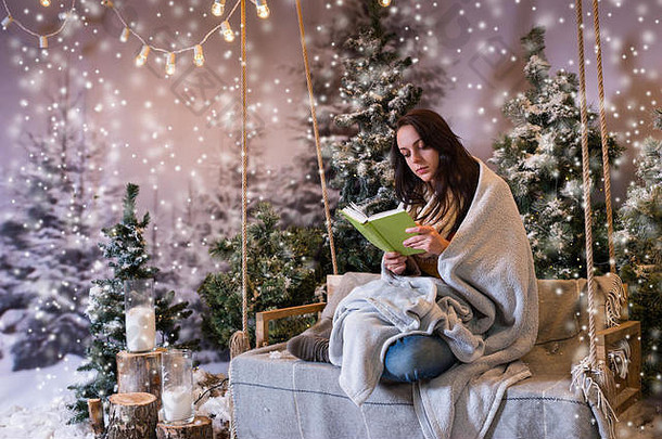 浪漫的年轻的女人阅<strong>读书</strong>坐着摇摆不定的包装温暖的毯子白雪覆盖的公园云杉<strong>树下</strong>雪