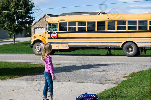 年轻的女孩挥舞着再见黄色的学校公共汽车