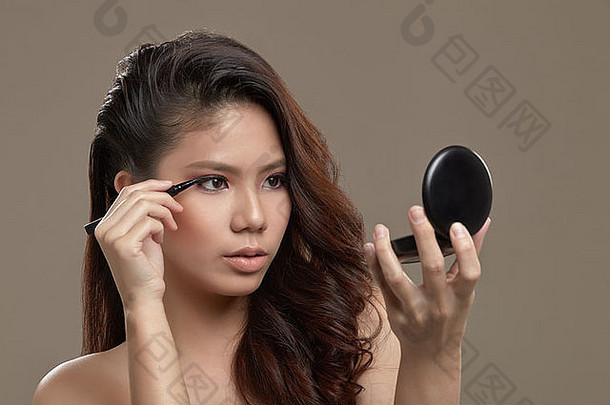 女亚洲使粉红色的眼睛影子持有液体眼睛衬管笔应用眼睛衬管镜子