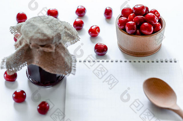 红色的成熟的樱桃小时Jar木勺子笔记本白色背景平躺食物概念