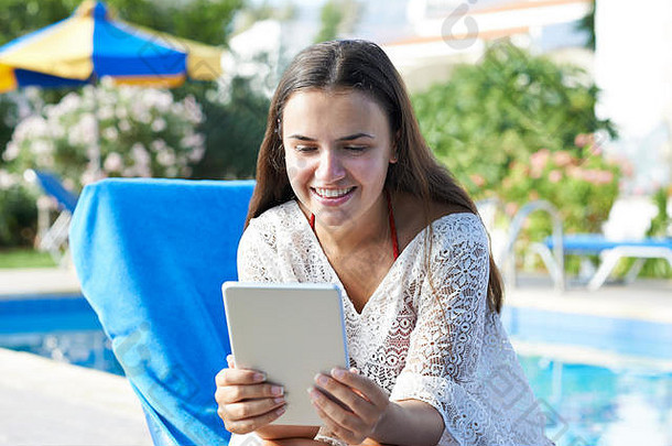年轻的女孩数字平板电脑放松游泳池假期