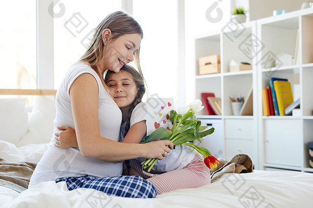 完整的长度肖像可爱的女孩拥抱怀孕了妈妈。给花母亲一天坐着舒适的床上早....复制空间