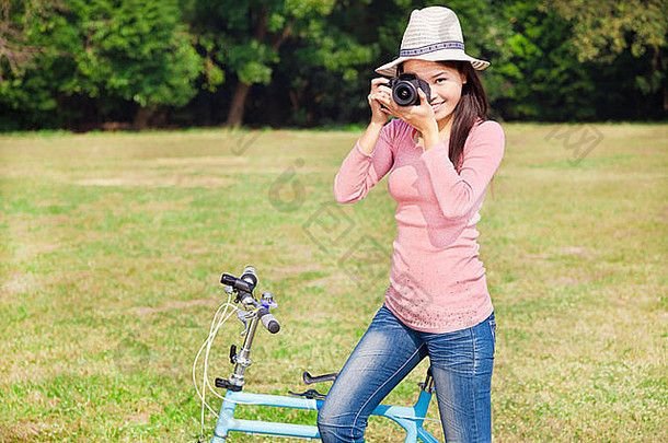 女摄影师持有相机坐着<strong>自行车</strong>
