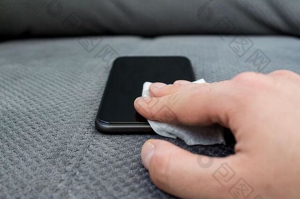 男人的手清洁智能手机屏幕消毒液喷雾消毒使灰色沙发