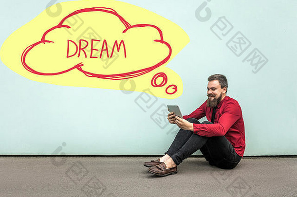 快乐有胡子的商人红色的衬衫坐着地板上持有数字平板电脑做梦黄色的云形状墙梦想