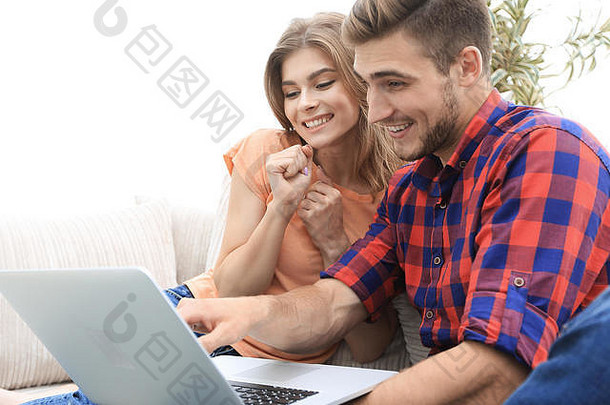 微笑年轻的夫妇移动PC坐着沙发上